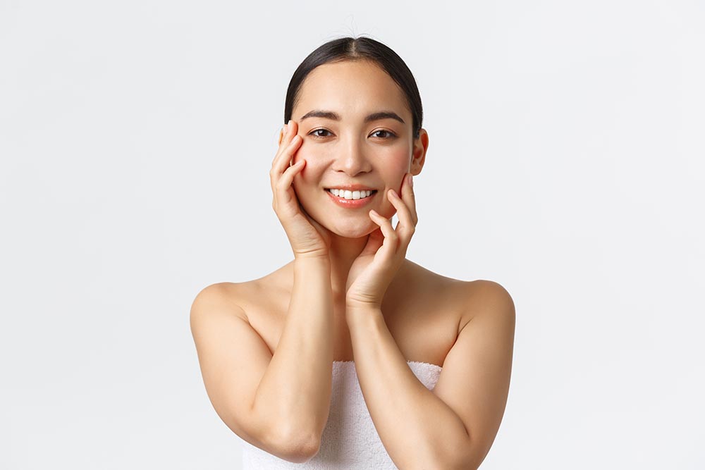 gorgeous sensual asian woman towel touching face smiling applying skincare products cosmetic procedure spa salon massaging face gazing camera happy white background