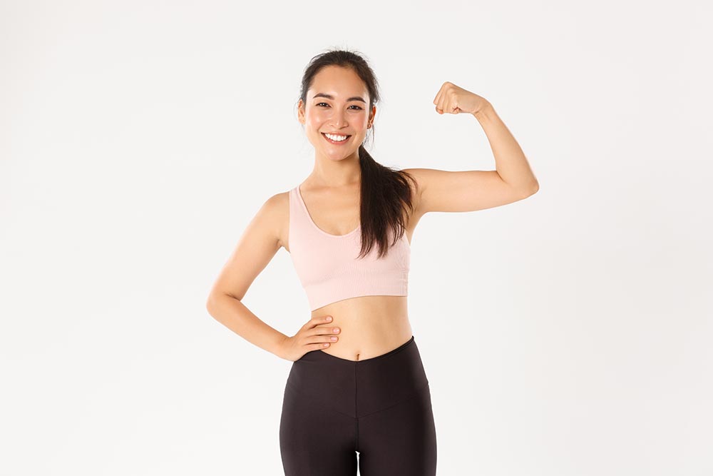 sport wellbeing active lifestyle concept portrait smiling slim strong asian fitness girl personal workout trainer showing muscles flexing biceps look proud white background